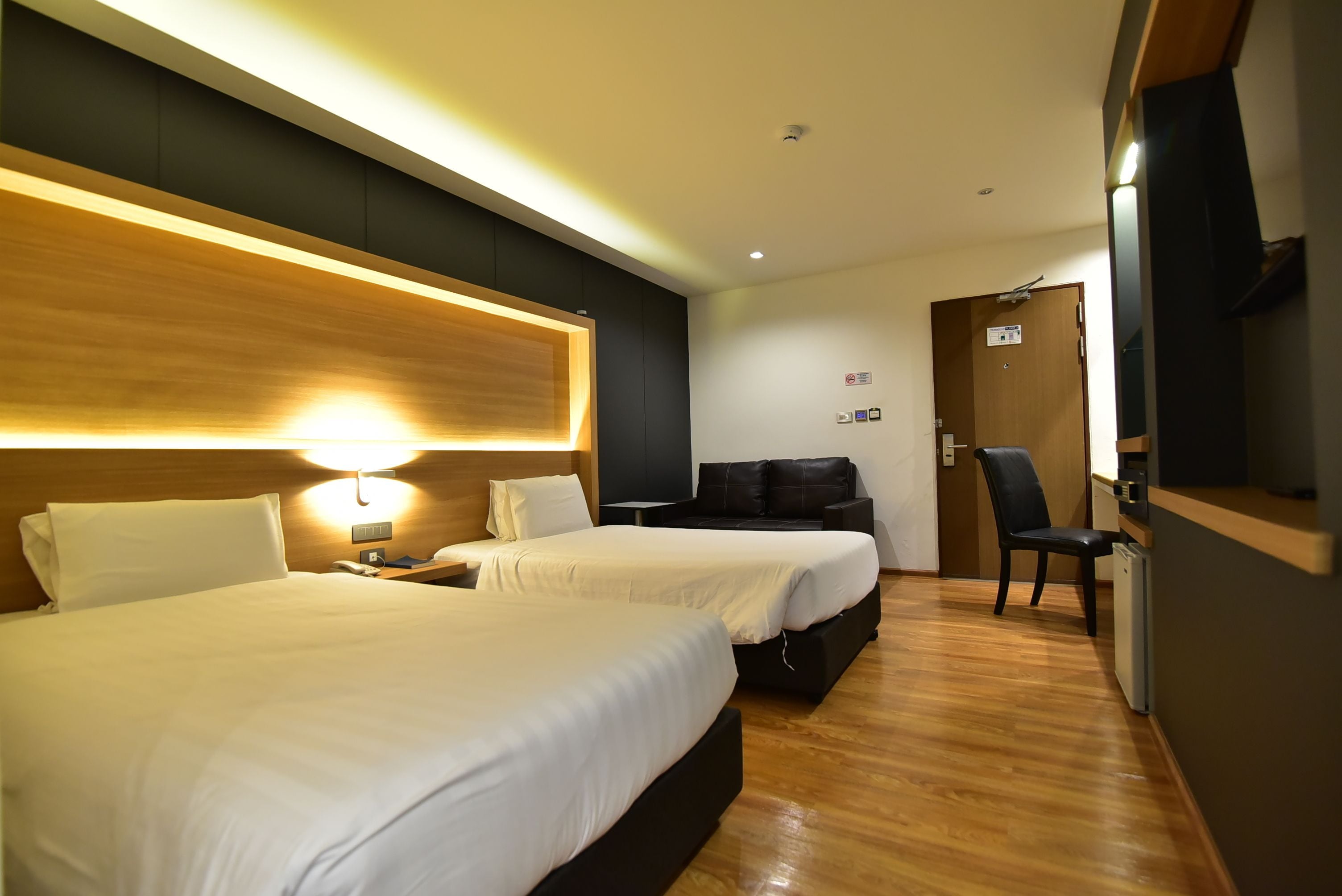 A hotel room with two beds, a desk, a chair, and a small kitchenette.
