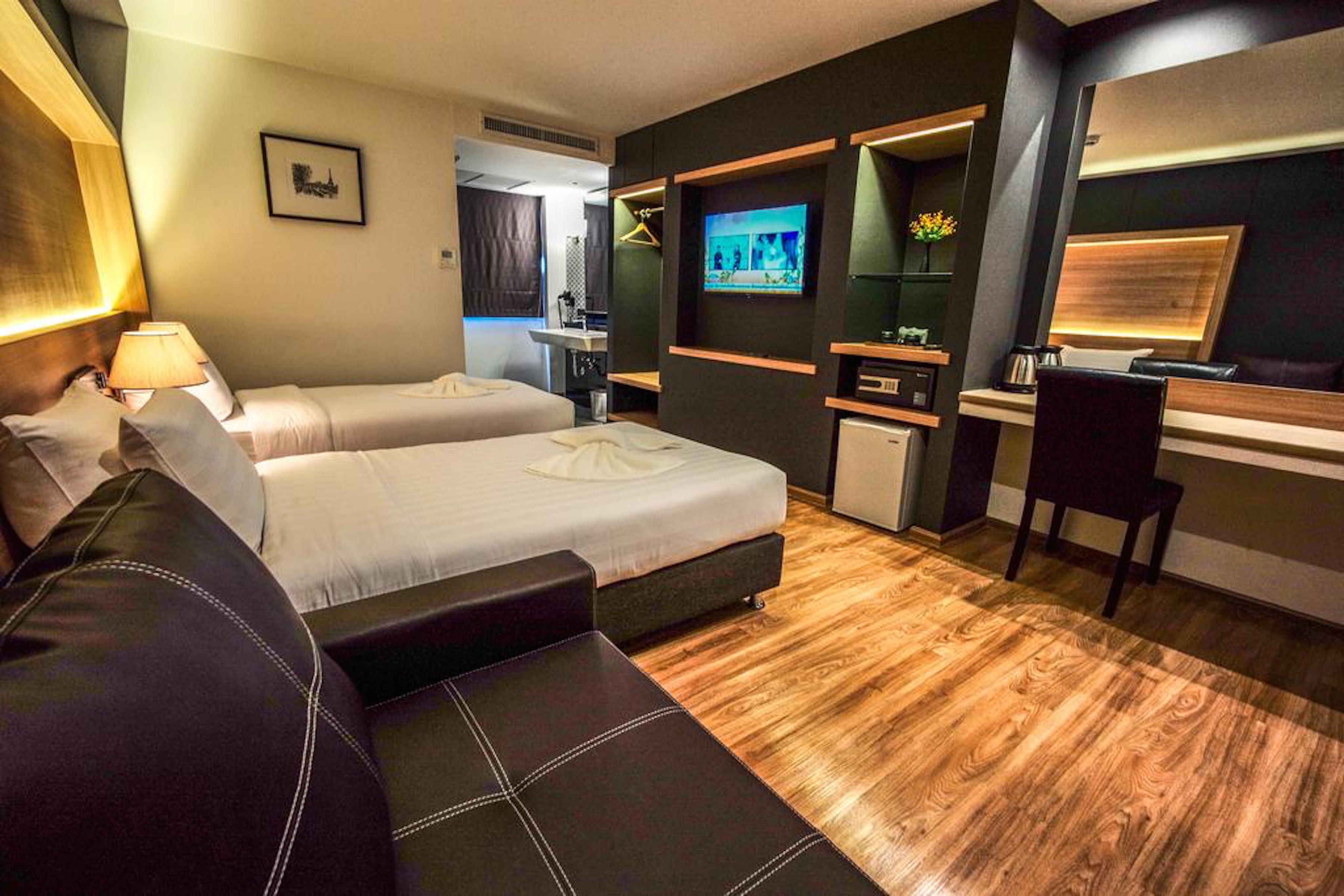 A hotel room with two beds, a desk, a TV, and a small kitchenette.