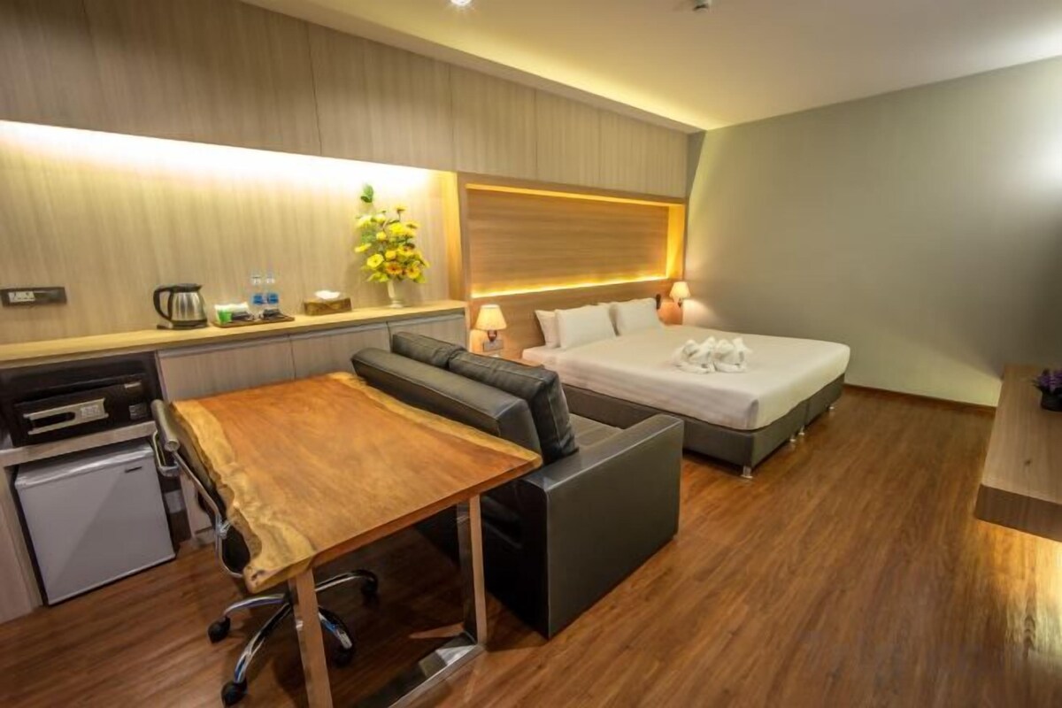 A compact hotel room with a kitchenette, a sofa bed, a single bed, and a small dining table.
