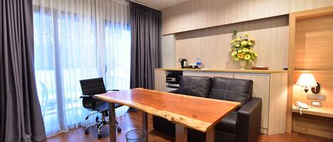 A modern hotel room with a wooden dining table, black leather sofa, and a small kitchenette.