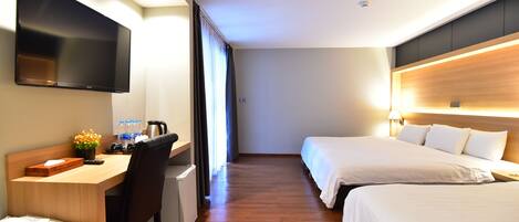 A hotel room with a wooden desk, a flat-screen TV, two beds, and a large window with curtains.
