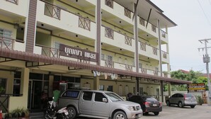 A multi-story building with a covered entrance, several parked cars, and a sign with Thai text. - Boonya Place (Chonburi)