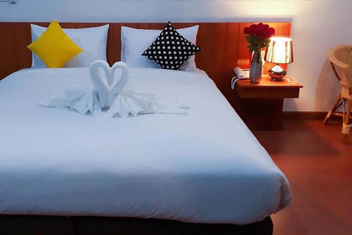 A hotel room with a neatly made bed, a wooden headboard, a nightstand with a lamp, and a chair.