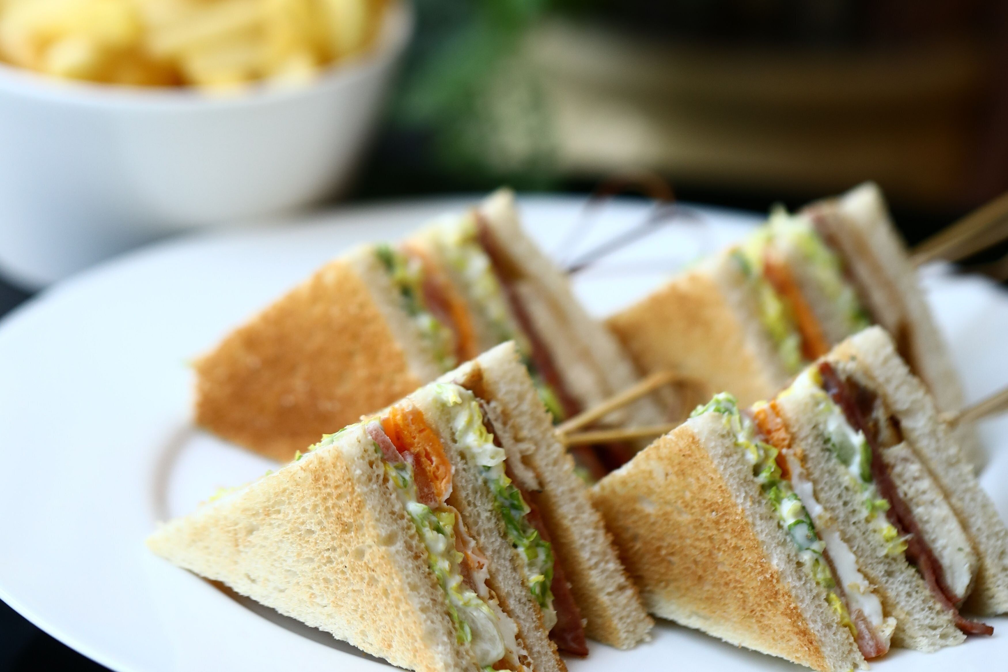 A plate with several sandwiches cut into triangles, accompanied by a bowl of fries in the background.