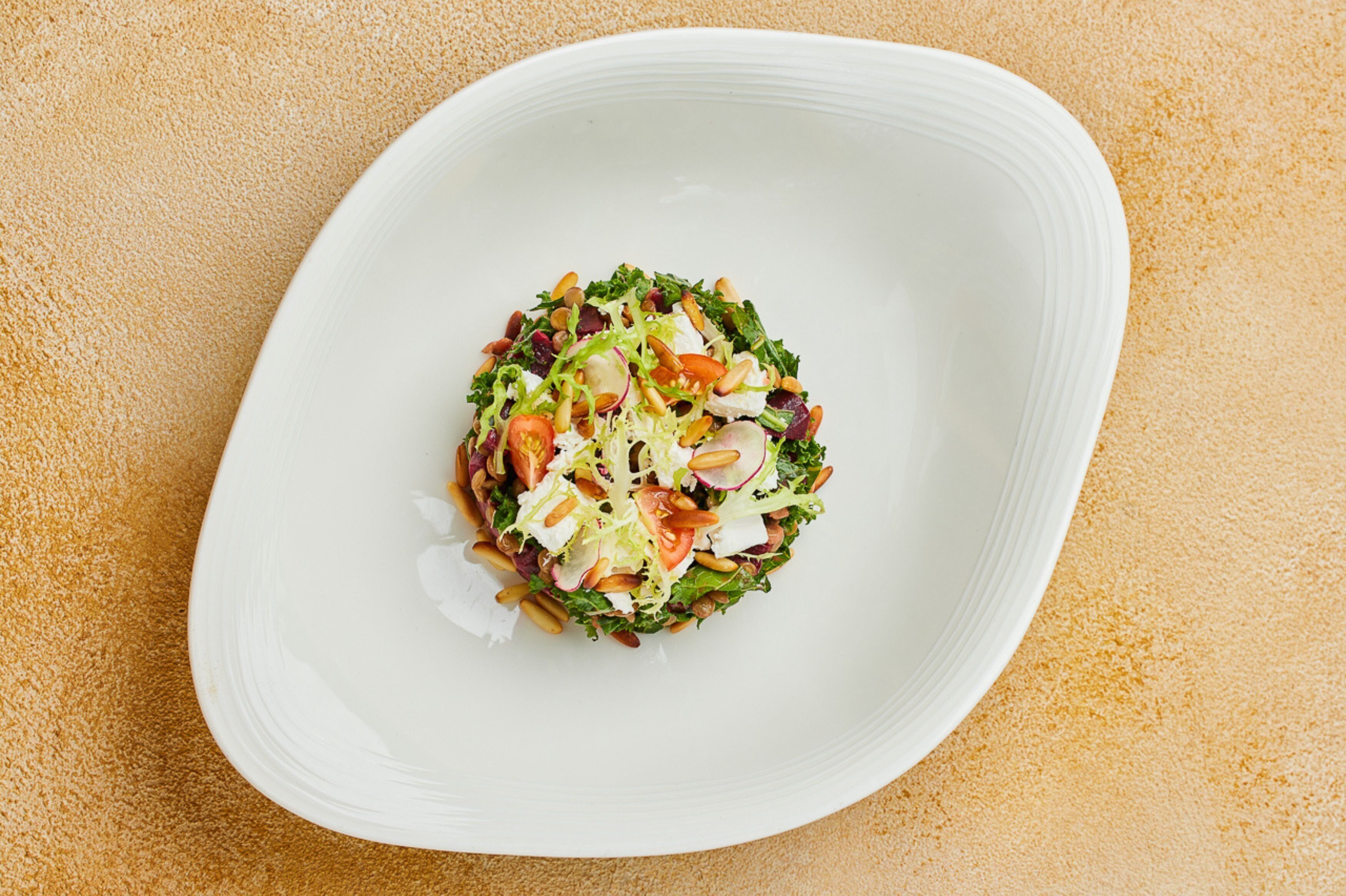 A white plate with a salad on a textured beige surface.
