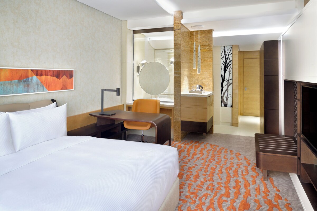 Une chambre d’hôtel comprenant un lit, un bureau, une chaise, une télévision et une salle de bain avec un miroir et un lavabo.