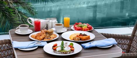 Mesa de comedor con alimentos para el desayuno y vista a la piscina.