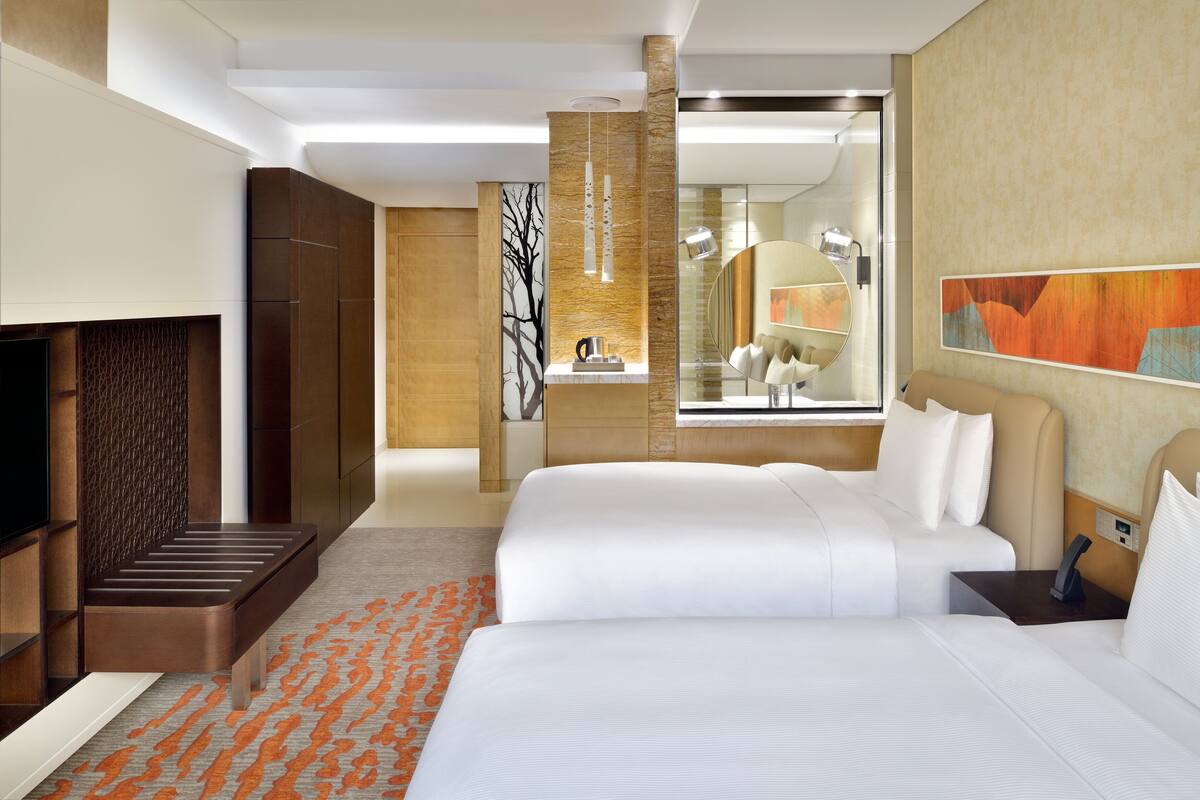 Una habitación de hotel moderna con una cama grande, televisión, zona de estar y baño con espejo y obras de arte.