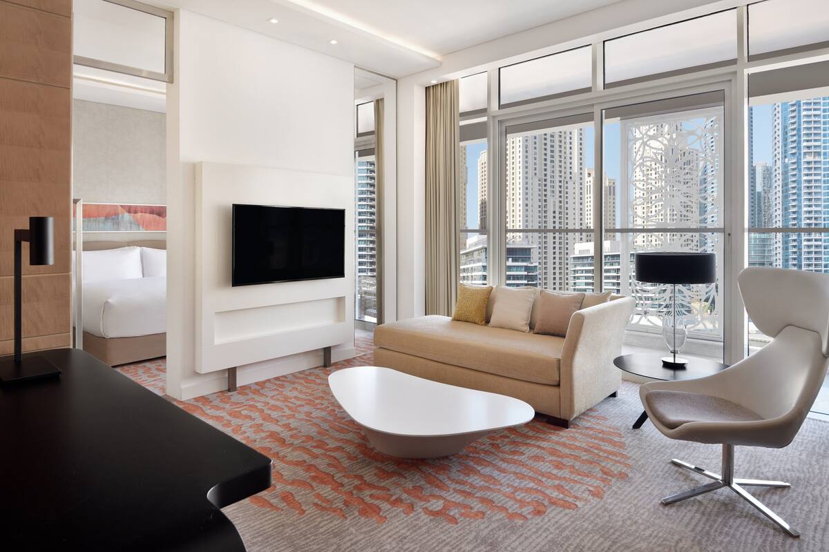 Una habitación de hotel moderna con un ventanal grande, un televisor de pantalla plana, un sofá, una mesita de café y una silla.