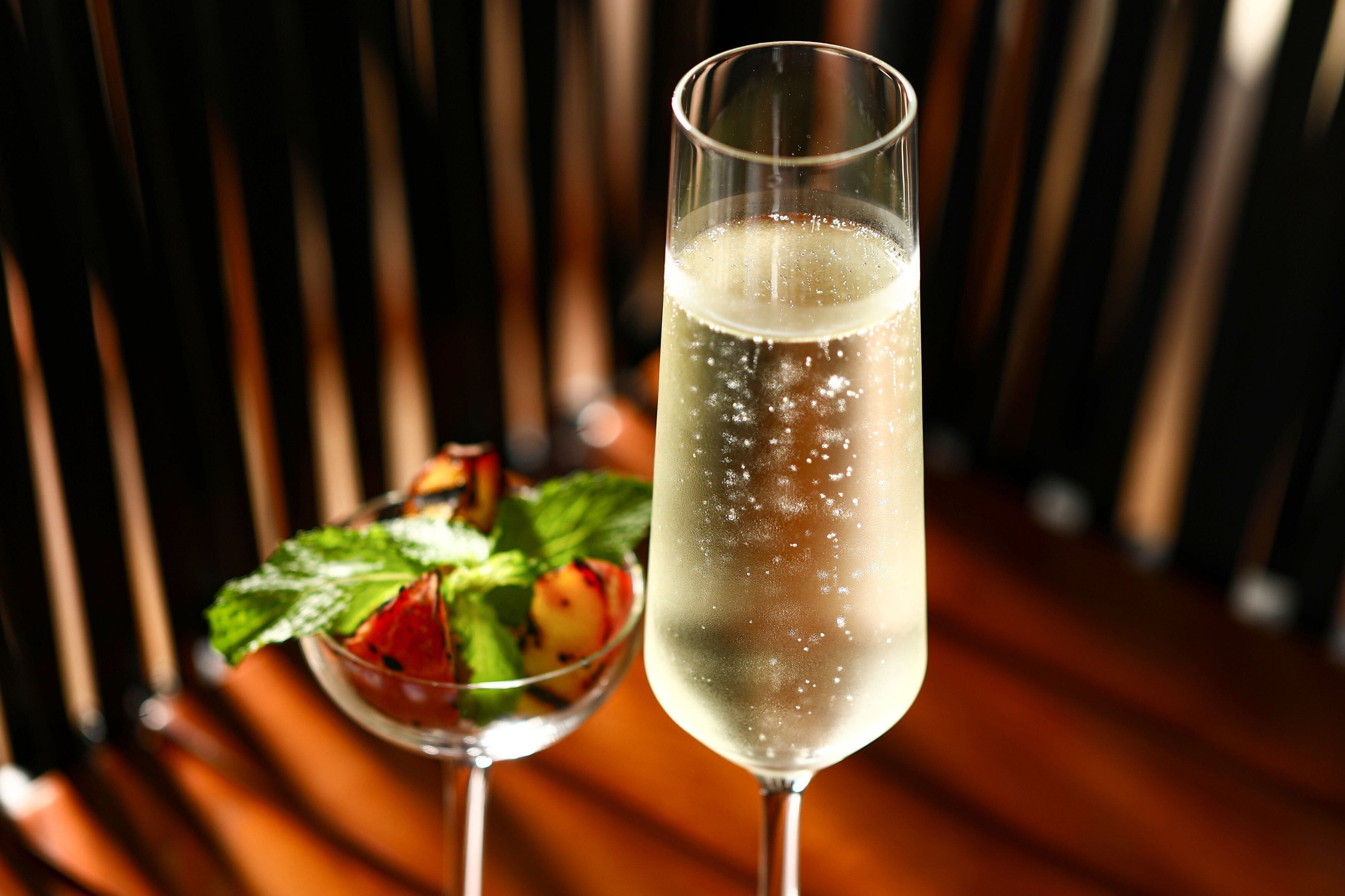 A glass of champagne with a fruit garnish and a cocktail in a glass.
