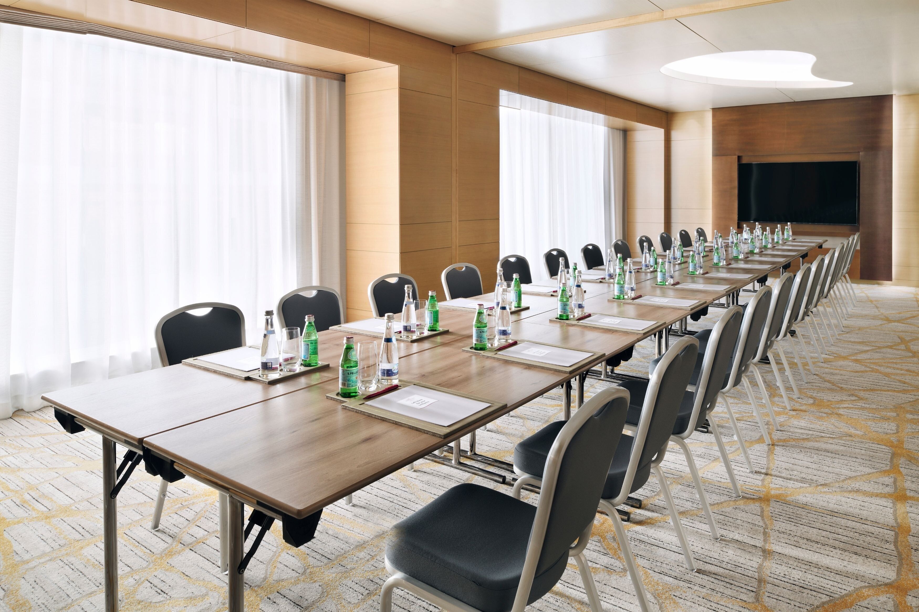A conference room with long tables, chairs, water bottles, and a large screen.