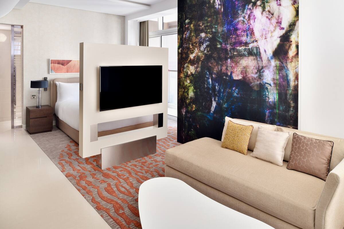 Una habitación de hotel moderna con cama, televisor, sofá y un cuadro abstracto grande.