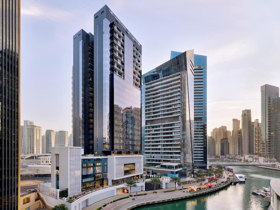 A modern urban skyline with high-rise buildings, a waterfront promenade, and a river.