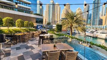 Une terrasse extérieure avec des tables et des chaises, offrant une vue sur un port de plaisance et le panorama de la ville.