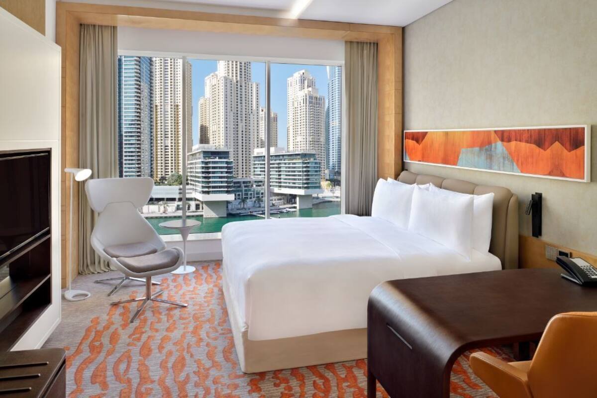 Una habitación de hotel con cama, escritorio, silla, televisor y vistas a edificios altos.