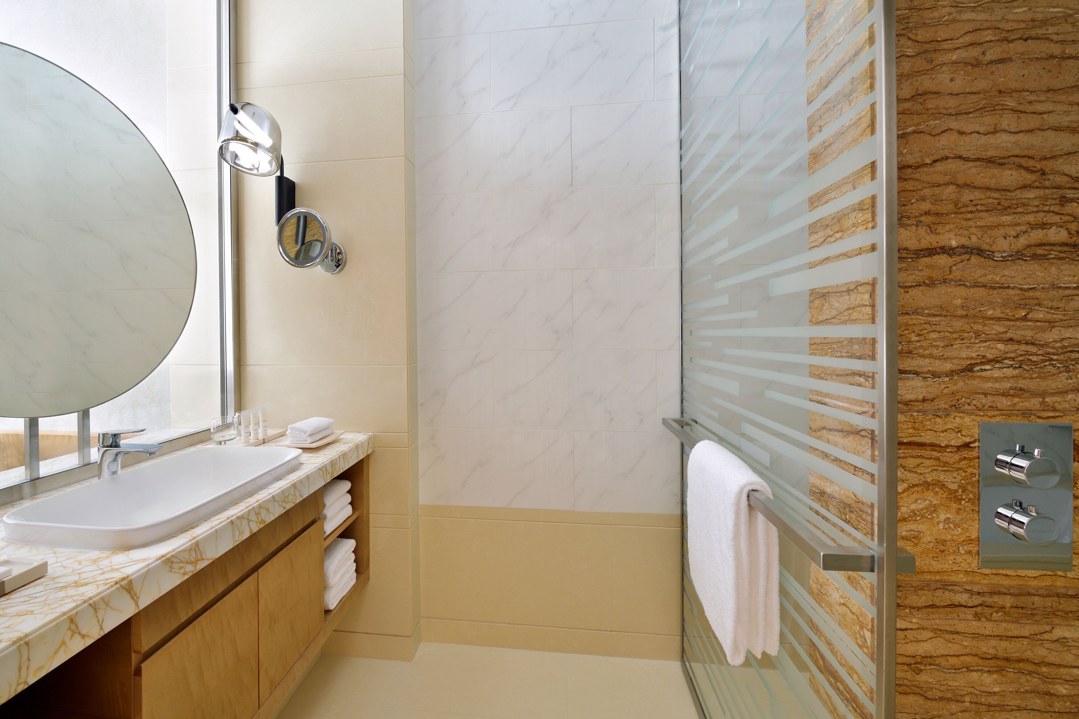 Un baño moderno con un espejo grande, un lavamanos, una ducha y un perchero para toallas.