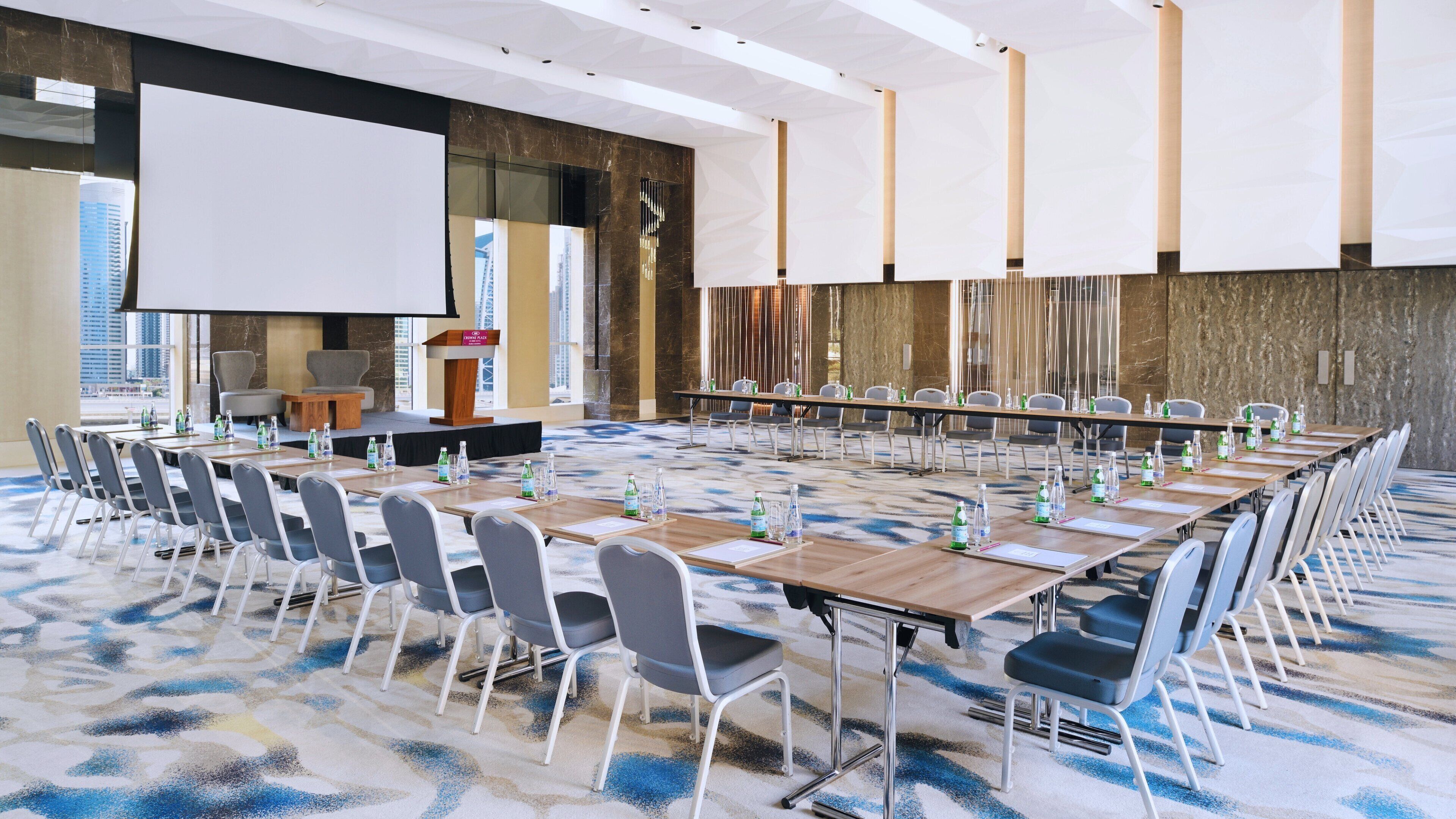 Ein Konferenzraum mit langem Tisch, Stühlen, einem Rednerpult und einer großen Leinwand.