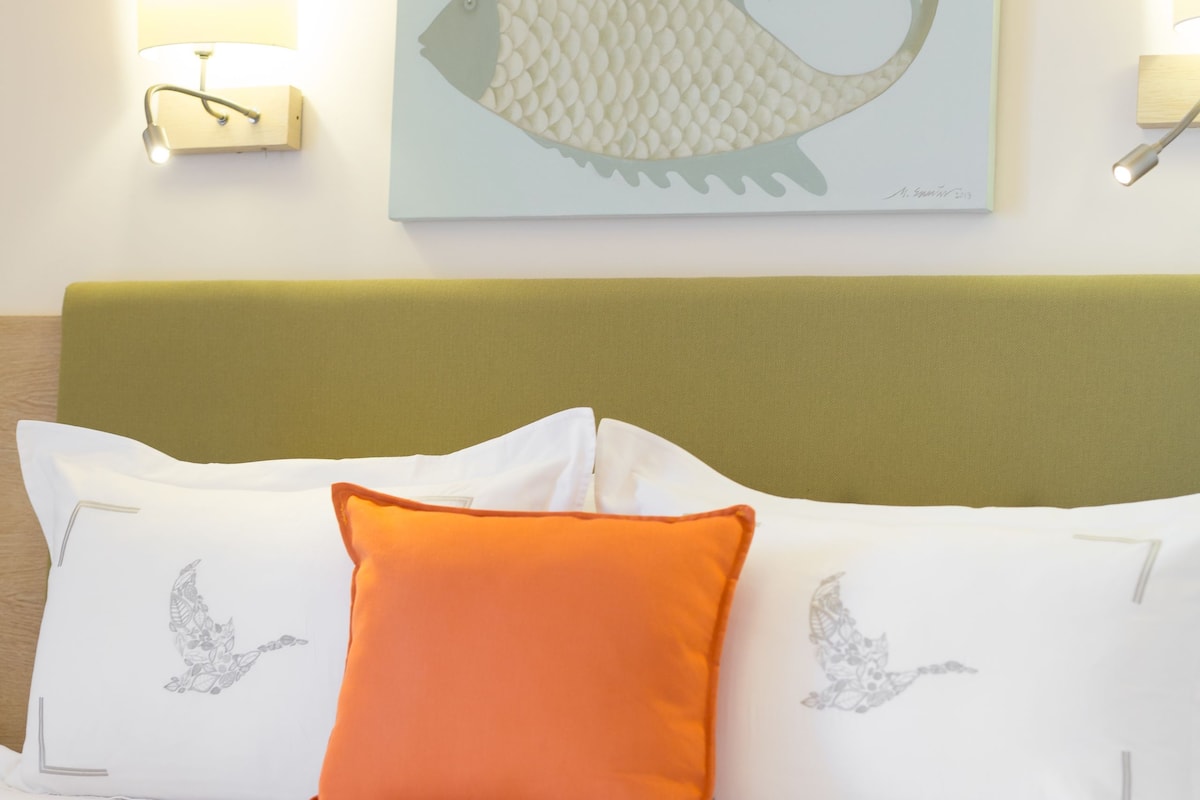 A hotel room with a bed, pillows, a wall-mounted fish artwork, and two wall sconces.
