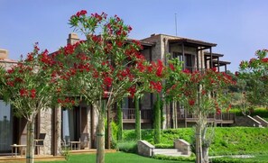 Un bâtiment à deux étages, doté d’une façade en pierre, de balcons et d’un jardin bien entretenu agrémenté de plantes à fleurs rouges.