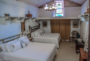 Ein Schlafzimmer mit zwei Betten, einer Kristalllüster, einem Fenster mit farbigem Glasdekor und einer Holzbalkendecke.