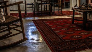 Un interior rústico con vigas de madera, un tapiz rojo con estampado y una araña.