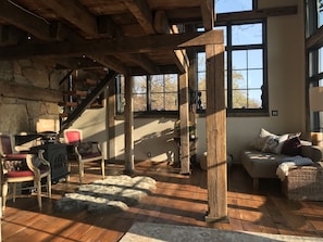 Cozy seating area with a sofa, chair, and small table, surrounded by a stone accent wall and a large window with a view.