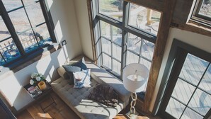 Ein Zimmer mit hohen Decken, Holzboden, großen Fenstern und einer eingebauten Bank mit Kissen.