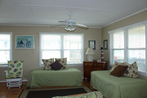 A bedroom with two beds, a ceiling fan, a chair, and a painting on the wall. - OCEANFRONT! Fall dates still available (Folly Beach)
