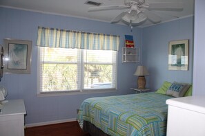 A bedroom with a bed, a nightstand, a lamp, a window with blinds, and a ceiling fan.