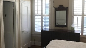 A bedroom with a large bed, a dresser, a mirror, and a door leading to another room.