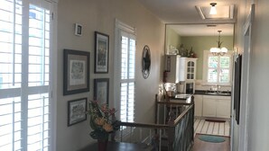 A dining area with a table and chairs, a kitchen in the background, and a hallway leading to a door.