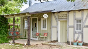 A rustic cottage with a porch, two chairs, and a sign that reads "Cottage." - Romantic Ava Haus Cottage. 3 minutes to Main! See our other 4 Ava Haus rentals. (Fredericksburg)