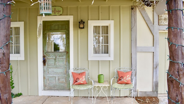 A porch with two white metal chairs, a green candle, and a door with a sign above it. - Romantic Ava Haus Cottage. 3 minutes to Main! See our other 4 Ava Haus rentals. (Fredericksburg)