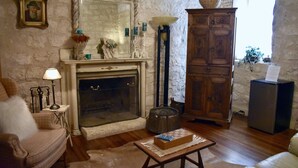 A cozy living room with a fireplace, a wooden cabinet, a cushioned armchair, and a small table with a chessboard.