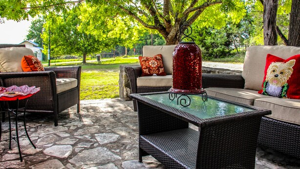 An outdoor patio area with wicker furniture, a glass-top table, and a decorative vase.