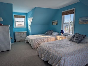 A bedroom with two beds, a dresser, a lamp, and a window with a view.