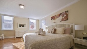 Quarto com cama grande, mesa de cabeceira, cômoda e um quadro na parede.