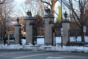 Une entrée fermée par un portail en fer forgé orné de motifs décoratifs et flanquée de statues, le tout entouré de neige.