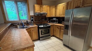 A kitchen with wooden cabinets, a stainless steel refrigerator, a stove, and a microwave. - Girdwood Alaska rental near ski resort. Customers rave: so cute, clean and cozy! (Anchorage)