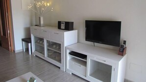 Una sala moderna con televisor de pantalla plana, mueble blanco para entretenimiento y una pequeña mesa con un florero.