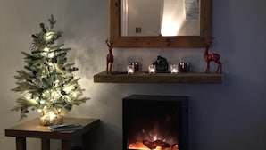 Una sala acogedora con chimenea, un pequeño árbol de Navidad decorado y un espejo sobre la repisa.