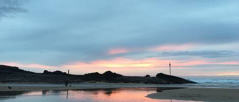 A beach with a calm sea, rocky outcrops, and a clear sky.