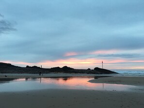 A beach with a calm sea, rocky outcrops, and a clear sky.