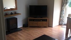 Una sala de estar con televisión de pantalla plana sobre un soporte de madera, chimenea y sofá.