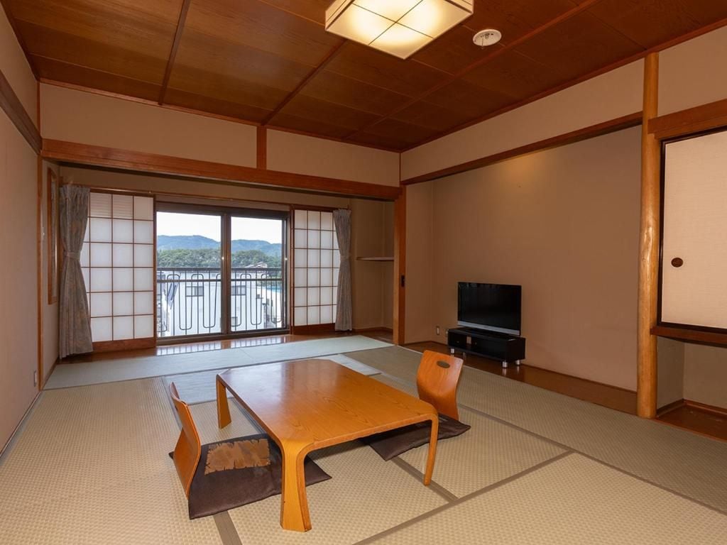 Una habitación tradicional japonesa con suelo de tatami, un fusuma con vistas, un televisor y una mesa de madera.