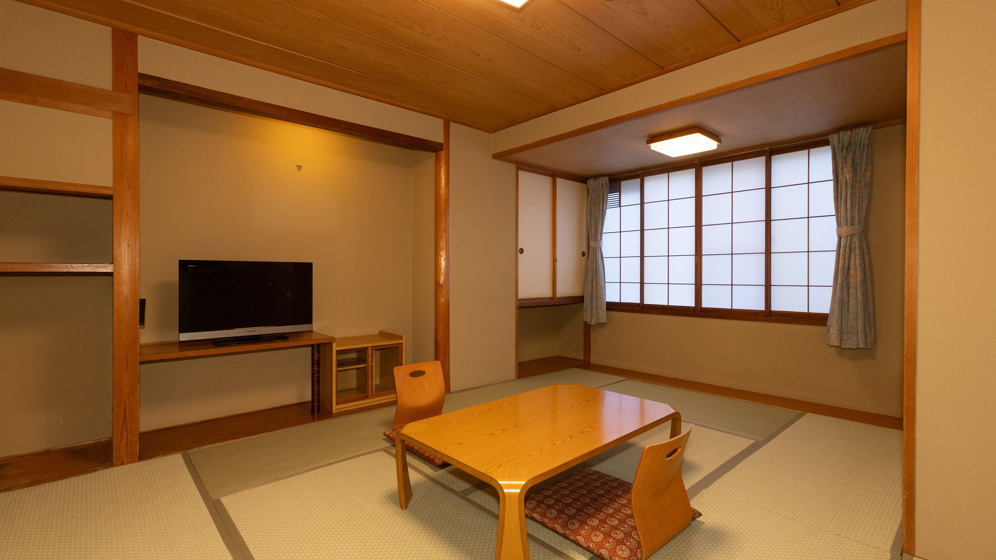 A traditional Japanese-style room with tatami flooring, a low wooden table, a television, and sliding doors.