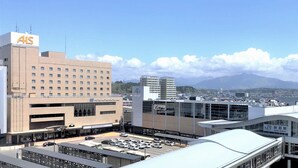 A hotel with a prominent 'ALS' sign, a parking lot, and a view of mountains in the background. - Hotel Metropolitan Akita (Akita)