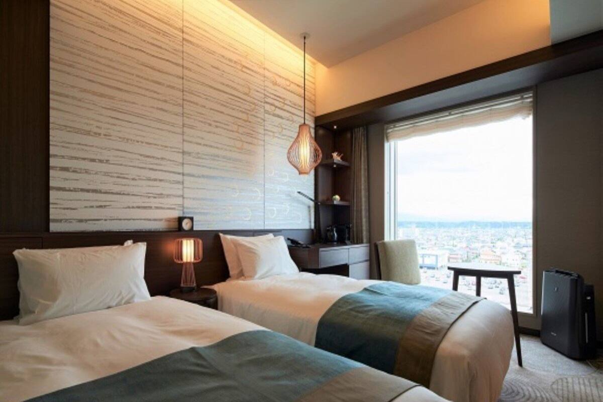 Une chambre d’hôtel avec deux lits, une grande fenêtre donnant sur la ville, un bureau et une chaise.