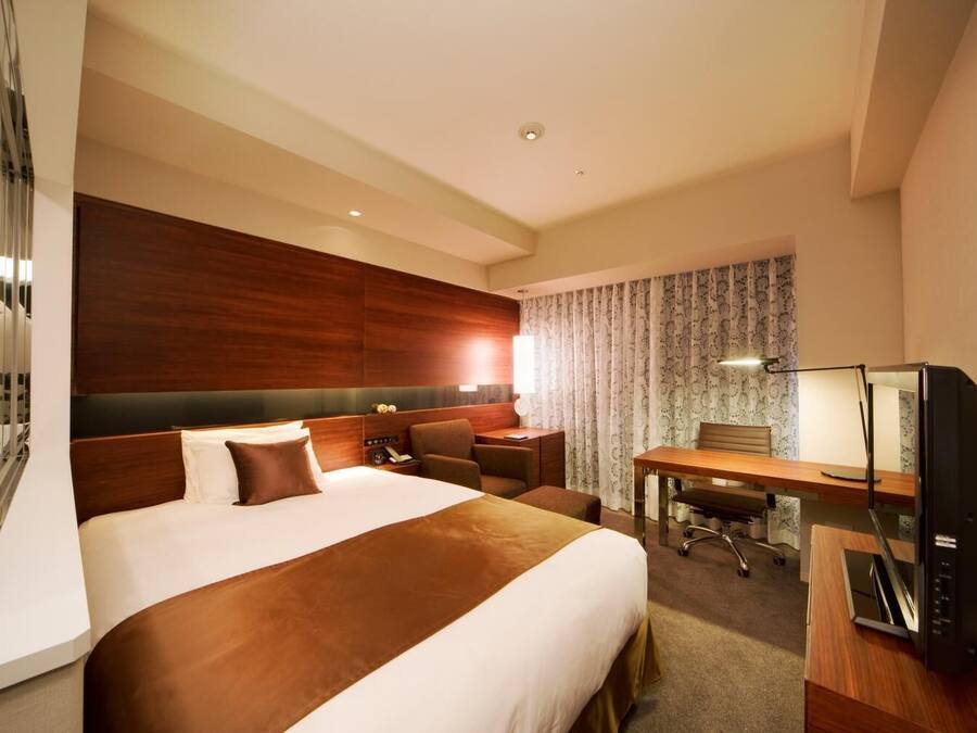 A hotel room with a large bed, a desk, a chair, a TV, and a mirror.