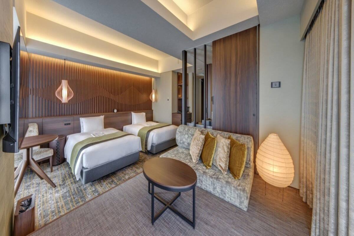 Une chambre d’hôtel moderne avec deux lits, un canapé, une petite table et une lampe.